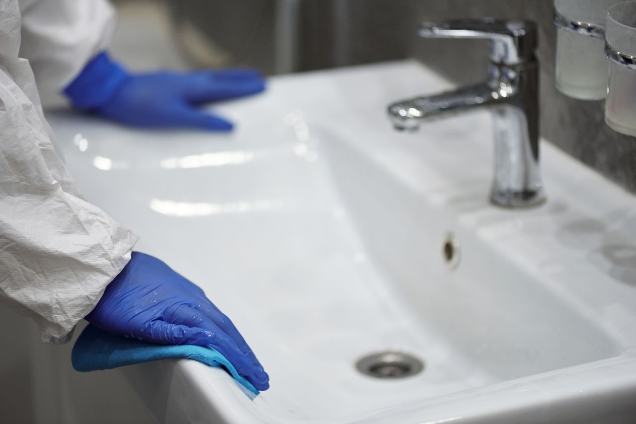 Gros plan d’un professionnel ganté nettoyant un évier pour des raisons d’hygiène.