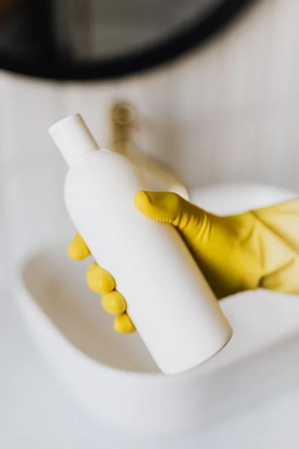 Des mains gantées de jaune nettoient un mur à l’aide d’une éponge et d’un vaporisateur.